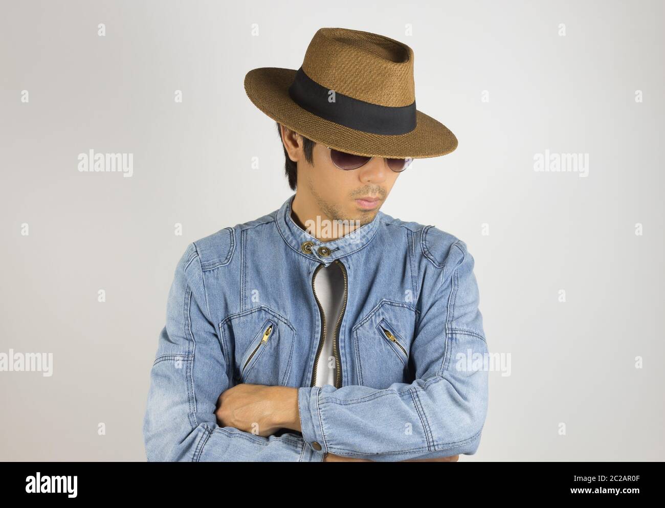 Young Asian Man en Jeans Denim Jacket veste ou porter des lunettes de soleil et chapeau en contre son bras. Denim ou jeans pour hommes Fashion sur fond gris Banque D'Images