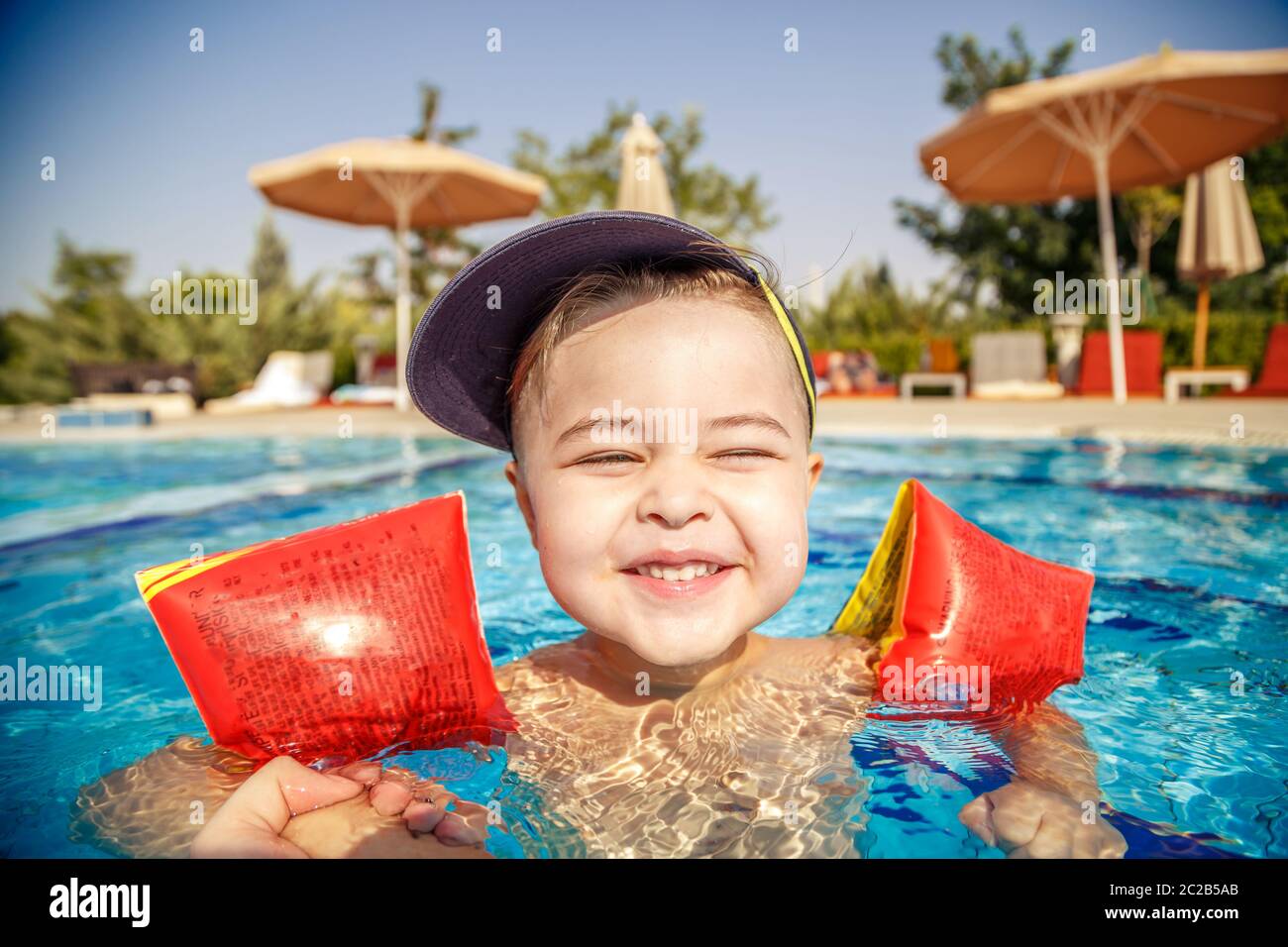 Un petit garçon apprend à nager dans la piscine en été avec l'appui de son père. Banque D'Images