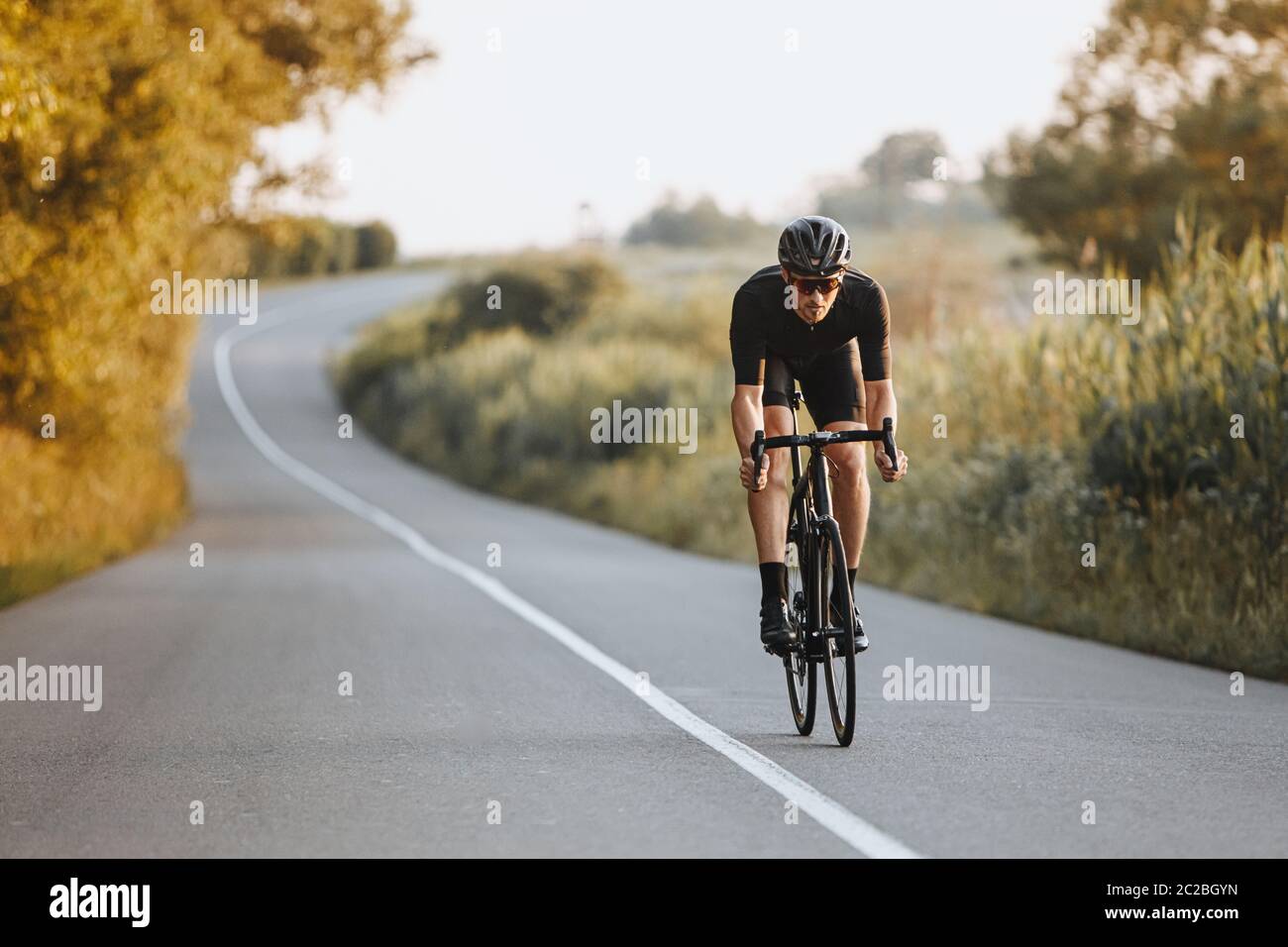 Cycliste professionnel, casque noir, lunettes de protection et casque d'activité, qui fait rouler dynamiquement le vélo sur route pavée avec un arrière-plan flou. Concept de Banque D'Images