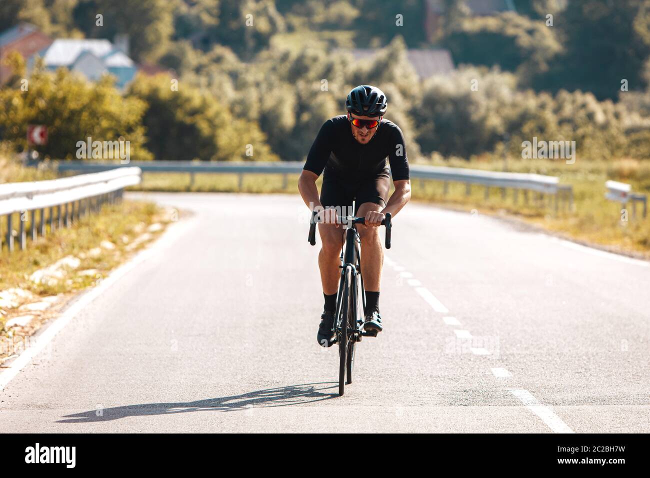 Vue avant de l'homme actif dans des vêtements de sport, casque noir et lunettes à miroir sur la nature à vélo professionnel pendant l'été. Concept d'actif Banque D'Images