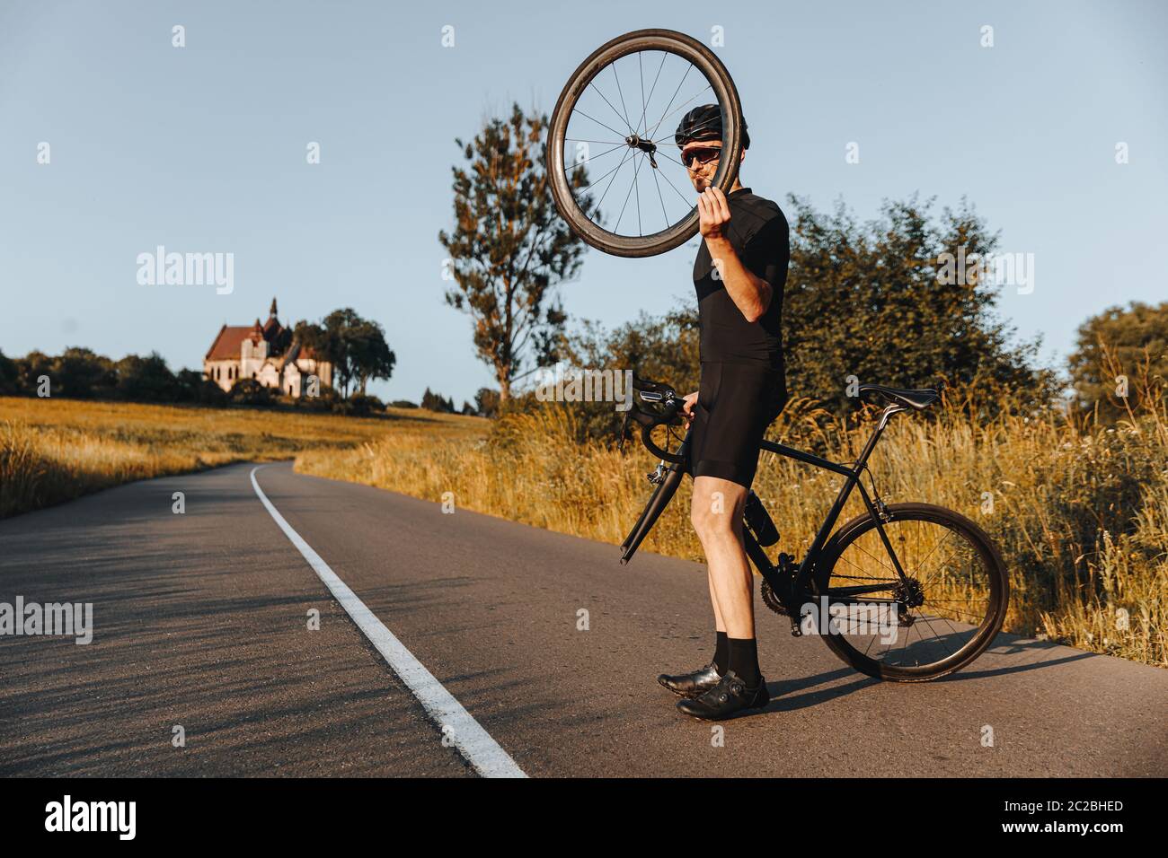 Homme mature en tenue active, casque de protection et lunettes miroir debout sur route pavée avec vélo cassé. Cycliste barbu tenant la roue à la main et Banque D'Images