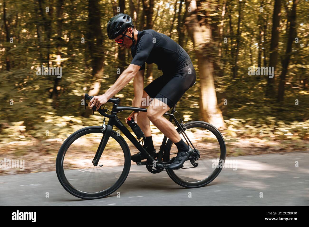 Athlète masculin robuste portant des vêtements actifs et un casque de protection, à vélo noir avec forêt verte. Concept de passe-temps sain et de tra régulier Banque D'Images