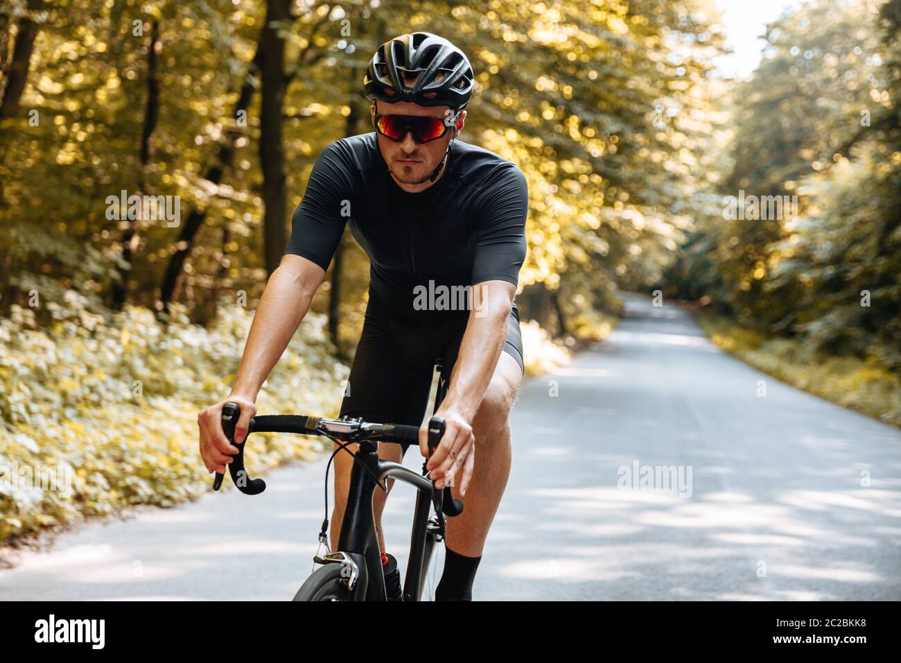 Homme barbu avec la forme du corps athlétique portant des vêtements de  sport et des lunettes à miroir, faisant du vélo dans la forêt verte.  Concept de frv actif et sain Photo