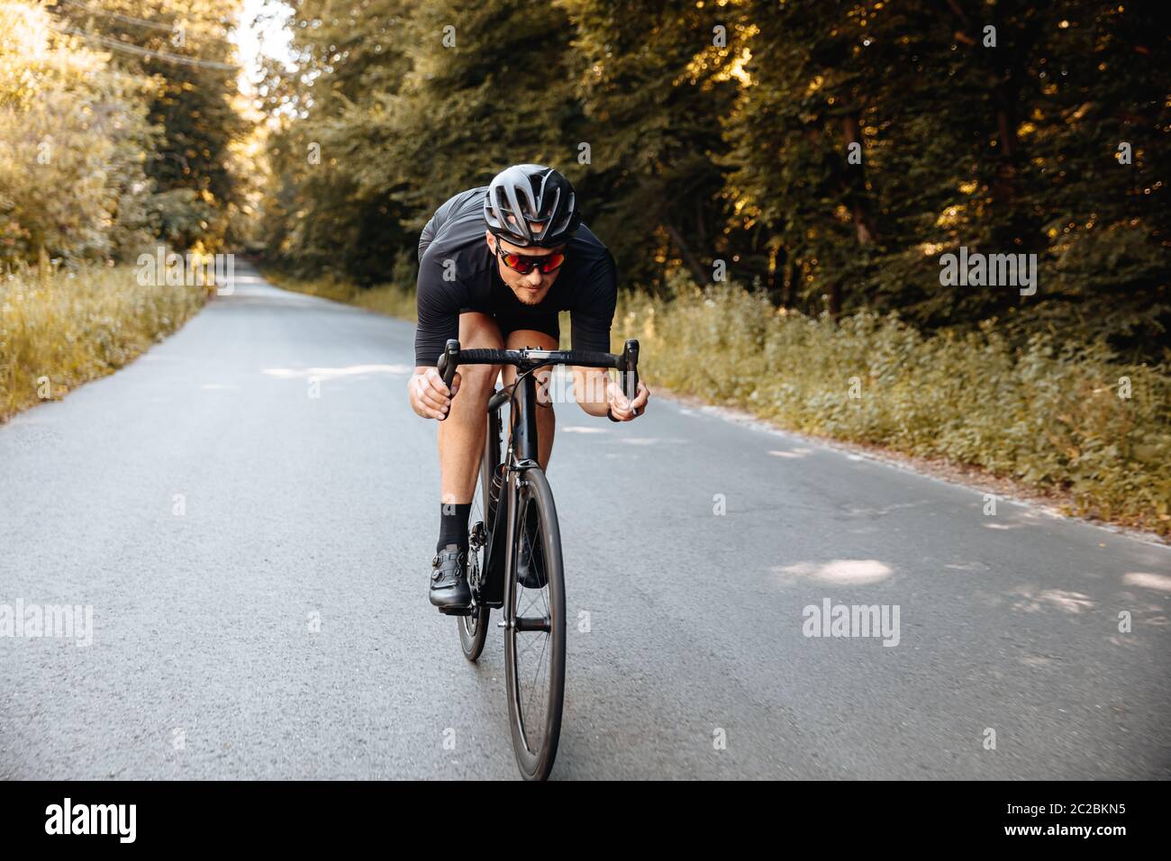 Homme sportif barbu dans un casque de protection et lunettes à miroir, à vélo dans une posture à moitié fléchie pour une meilleure vitesse. Sportif professionnel en pré-vêtement actif Banque D'Images