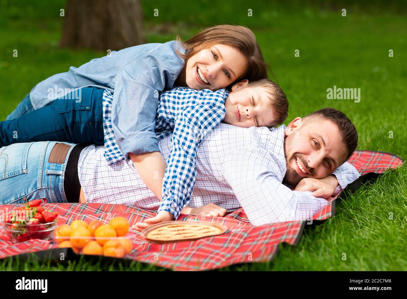 Famille joyeuse avec enfant allongé sur une couverture de pique-nique dans un pré vert Banque D'Images