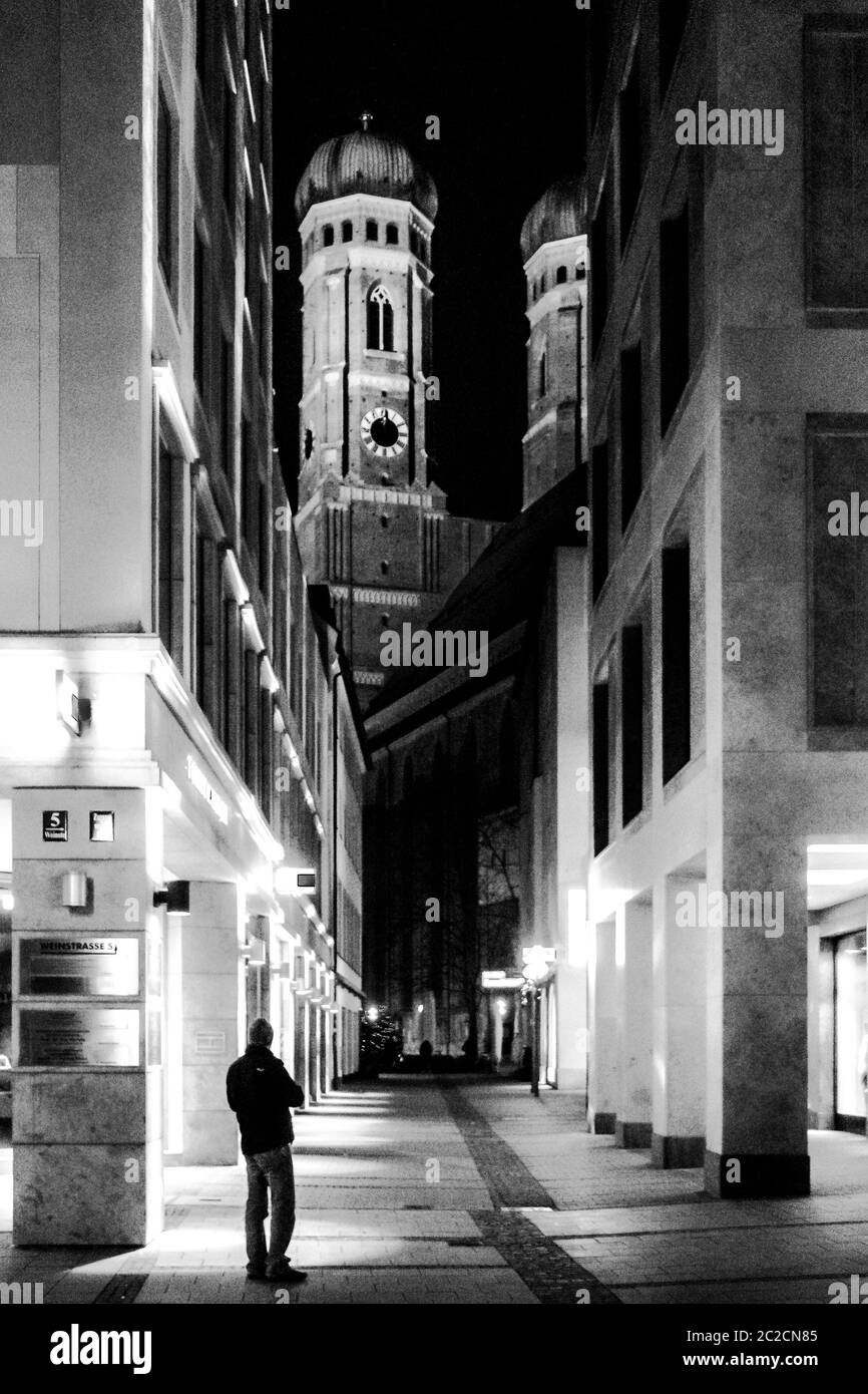 Un jeune homme qui regarde la Frauenkirche à Munich la nuit depuis une petite rue. Banque D'Images