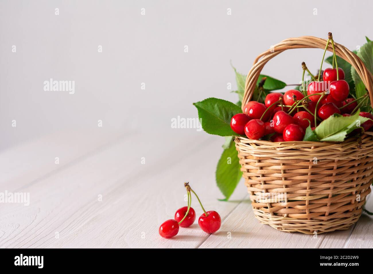 Cerises mûres juteuses dans un panier en osier sur fond de bois blanc Banque D'Images