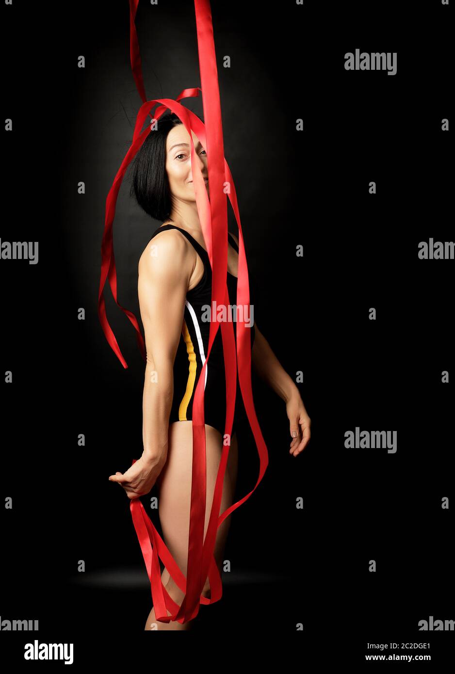 Jeune femme gymnaste de blancs avec des cheveux noirs d'apparence de rubans de satin rouge tours gratuits, des exercices de gymnastique sur fond noir Banque D'Images