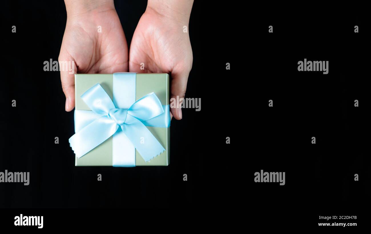 les femmes tiennent un petit cadeau enveloppé de ruban bleu sur fond noir Banque D'Images