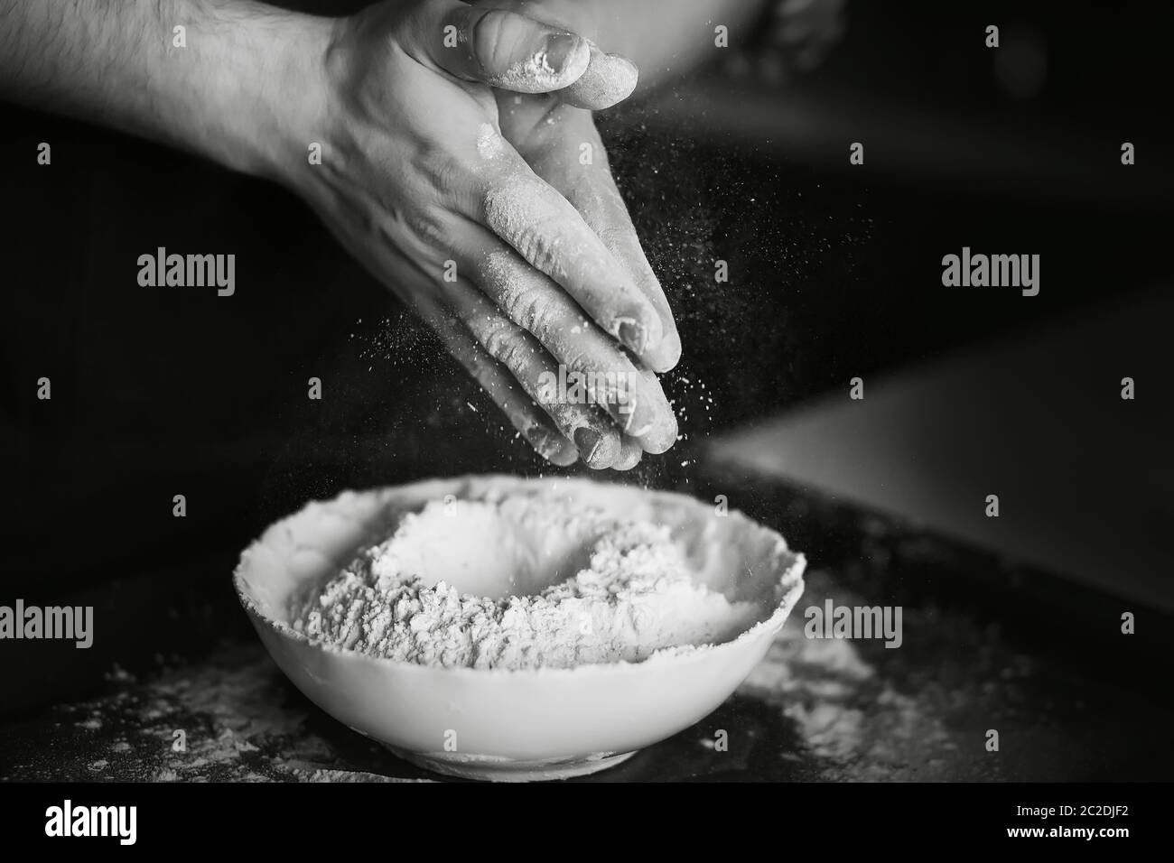 Image en noir et blanc du processus de cuisson de la pâte maison. Le cuisinier mélange la farine avec les autres ingrédients de l'assiette et secoue la farine Banque D'Images