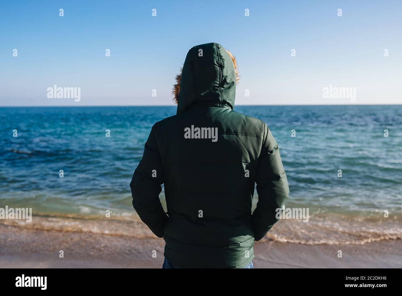 Jeune homme regardant la mer, vêtus de veste chaude avec capuche. Vue arrière. Banque D'Images