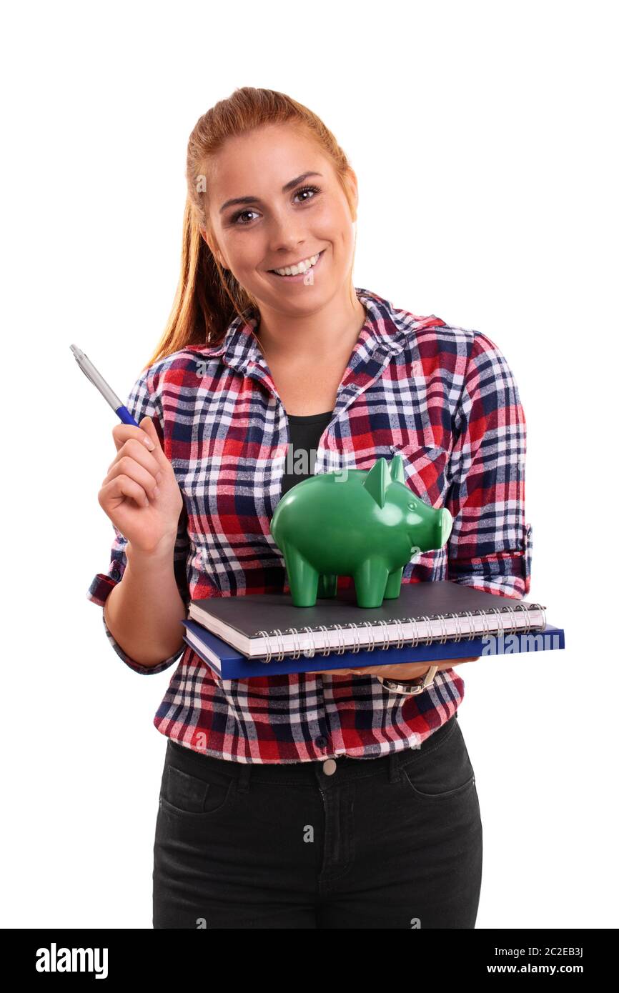 Smiling young student holding a piggy bank vert sur une pile de livres, en pointant avec un stylo, isolé sur fond blanc. Banque D'Images