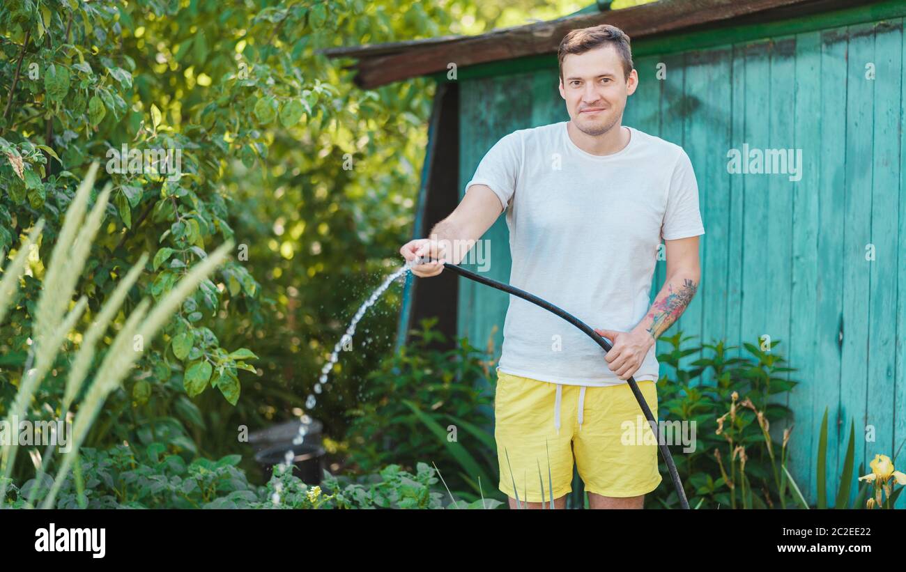 Homme arrosant le jardin à l'aide d'un tuyau. Un homme vaporise de l'eau  sur les légumes avec un tuyau d'arrosage. Un homme heureux avec un tuyau  s'occupe du jardin. Concept Photo Stock -