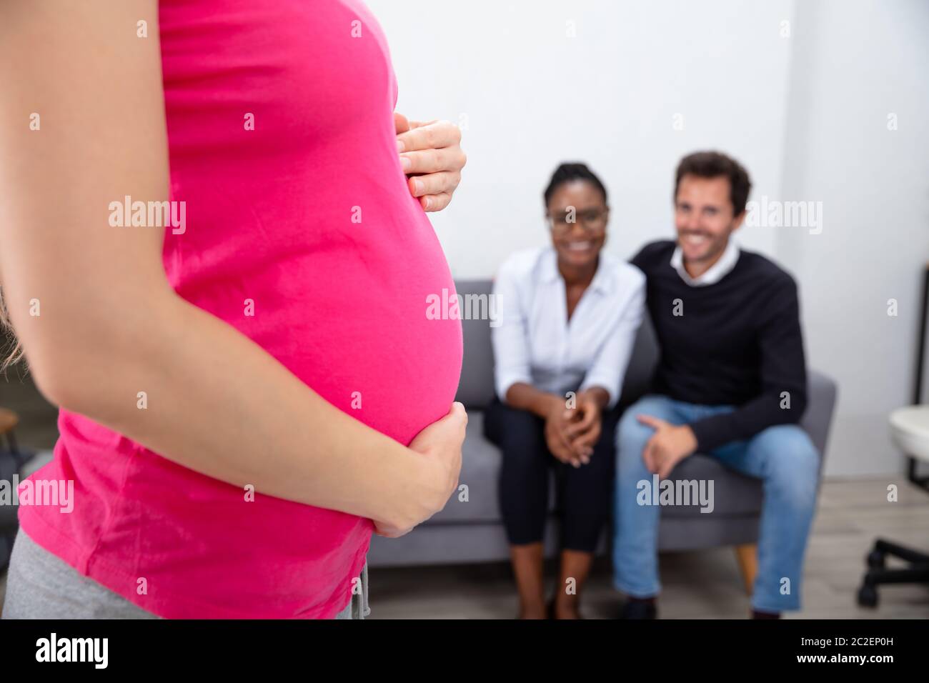 Femme enceinte de toucher son ventre's Woman standing in front of Smiling Young Couple Sitting Banque D'Images