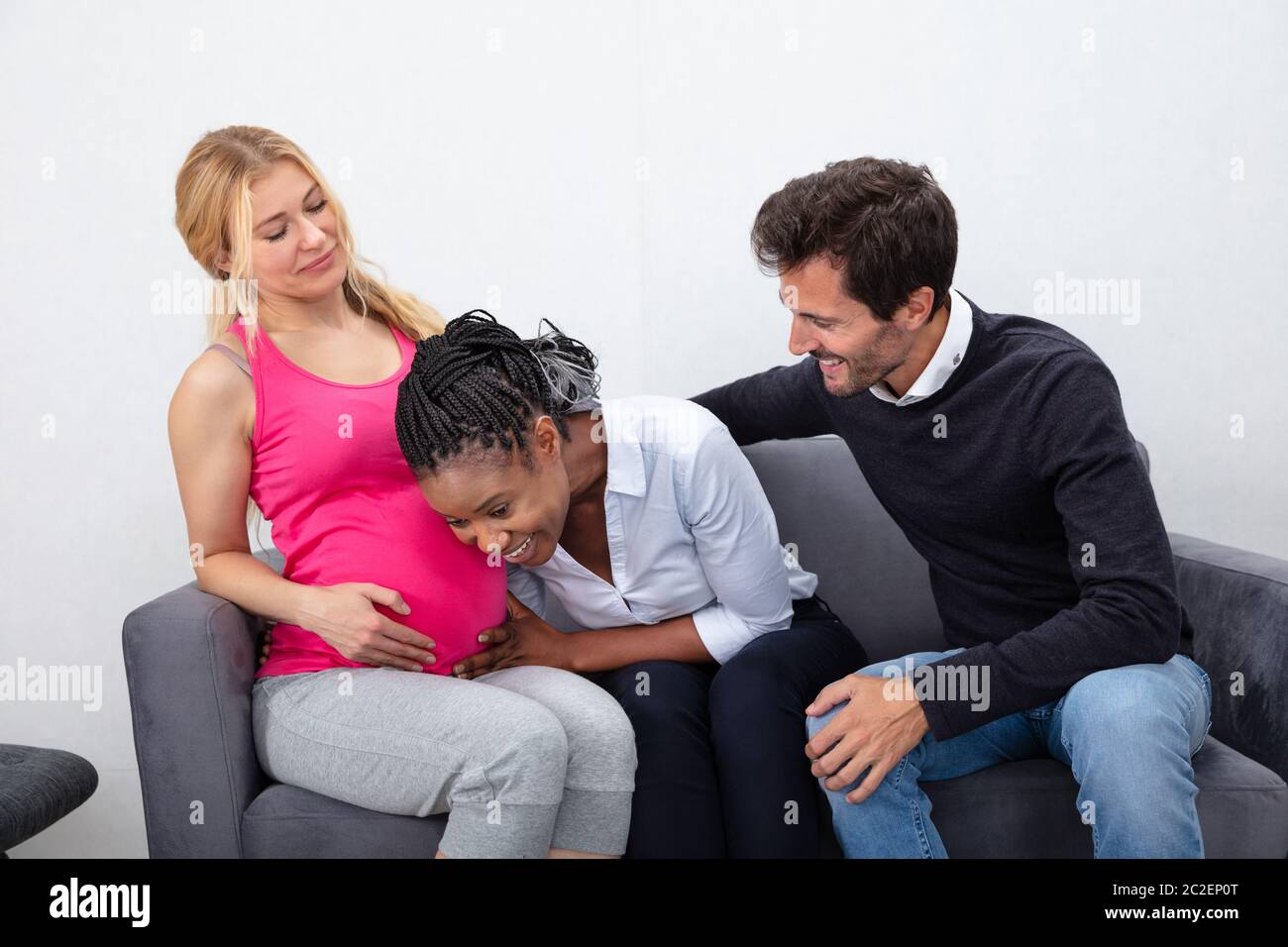 Smiling Young Man Looking At African ami à l'écoute de l'estomac de votre ami enceintes Sitting on Sofa Banque D'Images