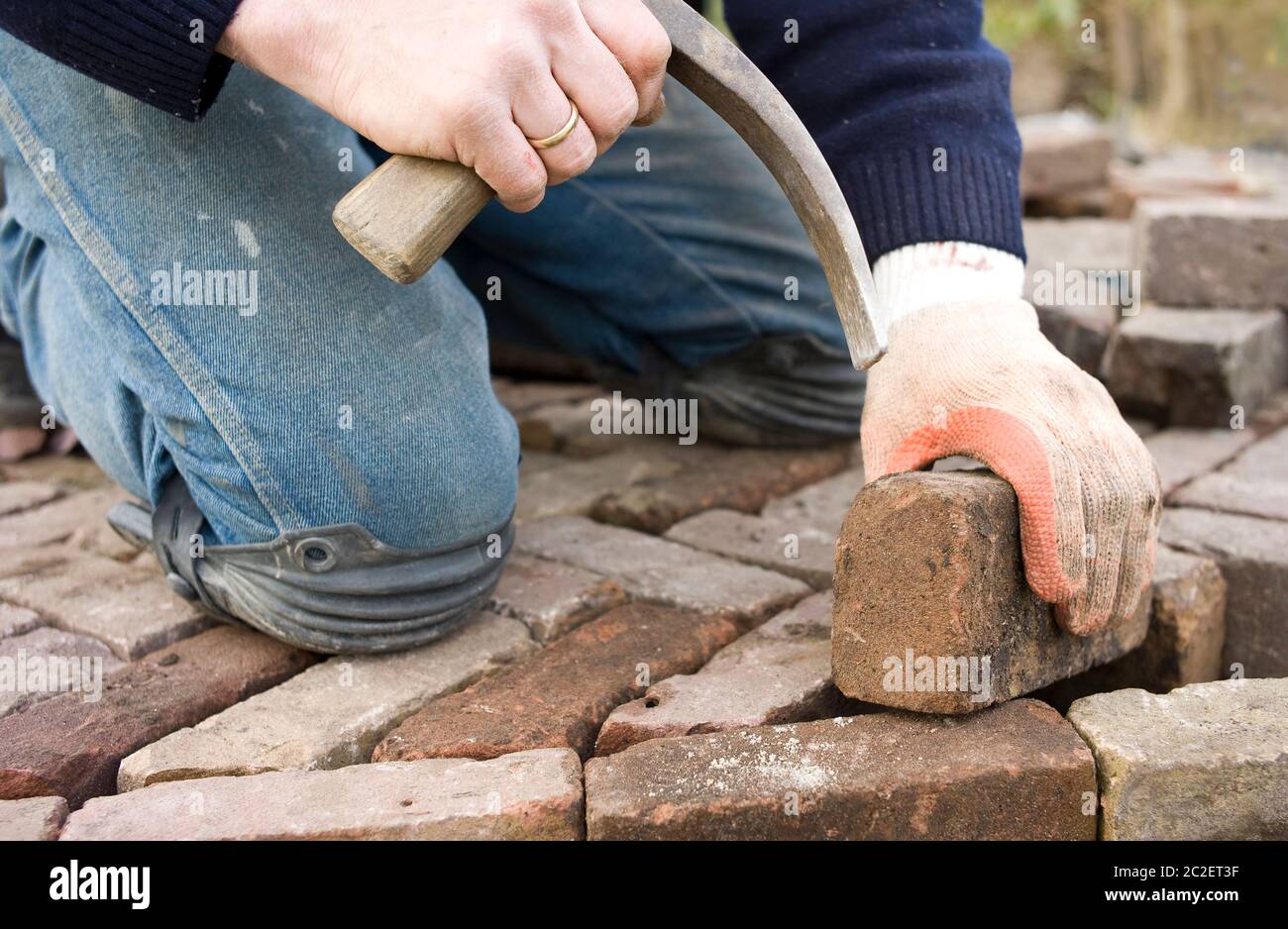 Les mains d'un ouvrier frappent un morceau de pierre avec un marteau de pierre pour le faire picher et pour placer des pavés de pierre. Banque D'Images