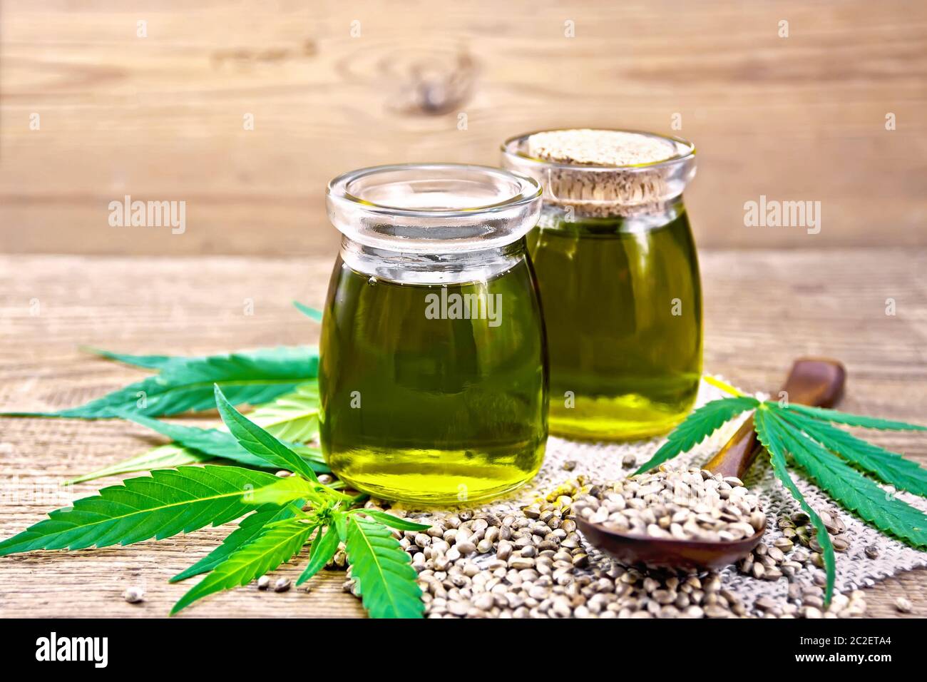 L'huile de chanvre dans deux pots en verre avec une cuillère et sur la table, feuilles de cannabis sur l'arrière-plan d'une vieille planche de bois Banque D'Images