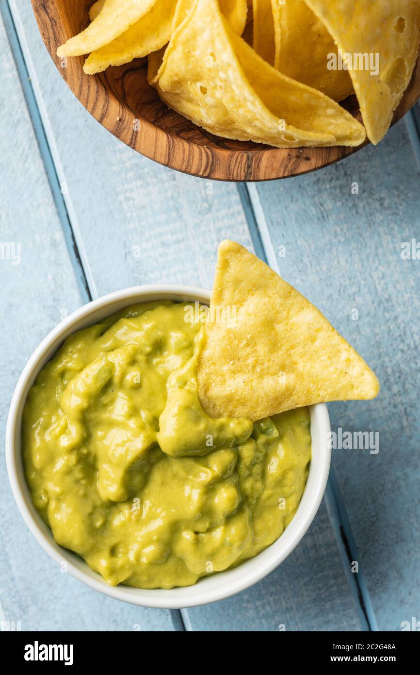 Croustilles de maïs et d'avocat trempette. Croustilles de maïs jaune et de guacamole en cuvette sur tableau bleu. Banque D'Images