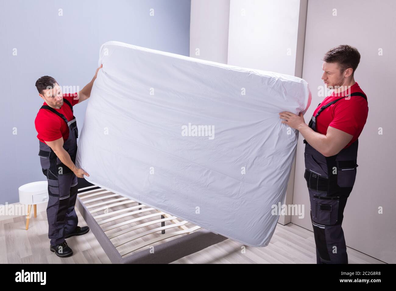 Deux hommes en uniforme des déménageurs professionnels de placer le matelas sur le lit dans la nouvelle maison Banque D'Images