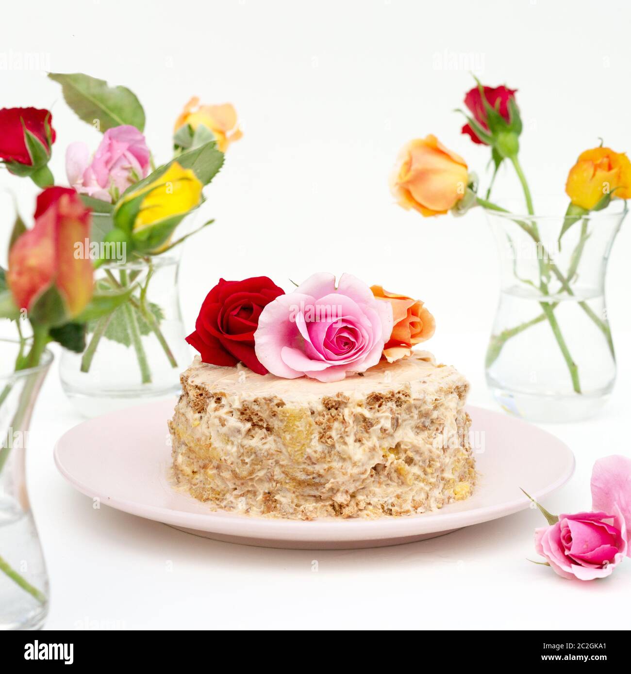 Petit gâteau maison décoré de roses vivantes sur fond blanc. Des roses multicolores sont sur la table dans un armudu en verre. Banque D'Images