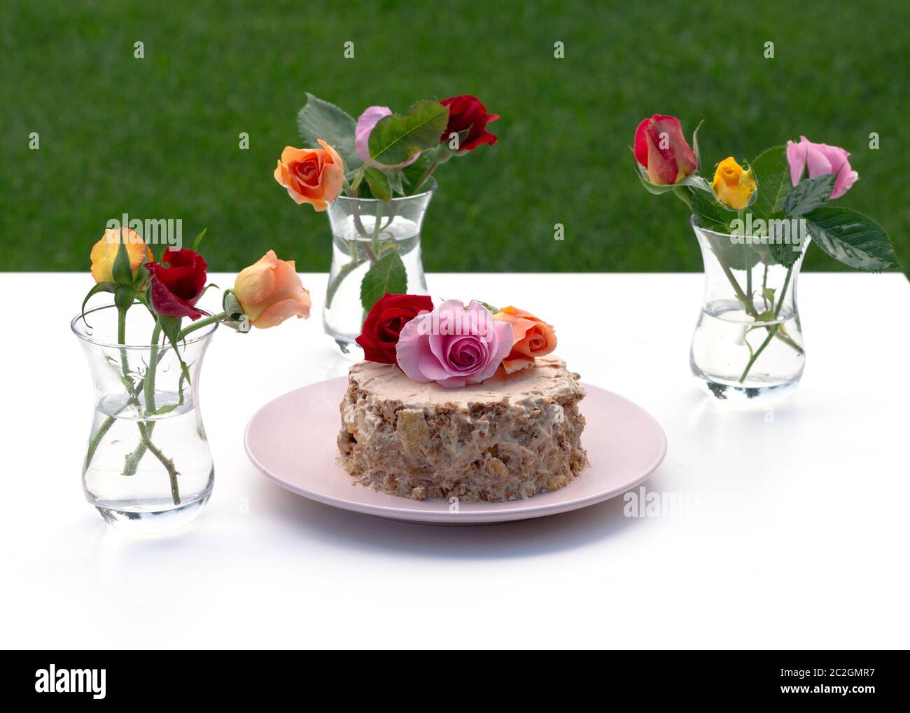 Petit gâteau maison décoré de roses vivantes sur fond blanc. Des roses multicolores sont sur la table dans un armudu en verre. Banque D'Images