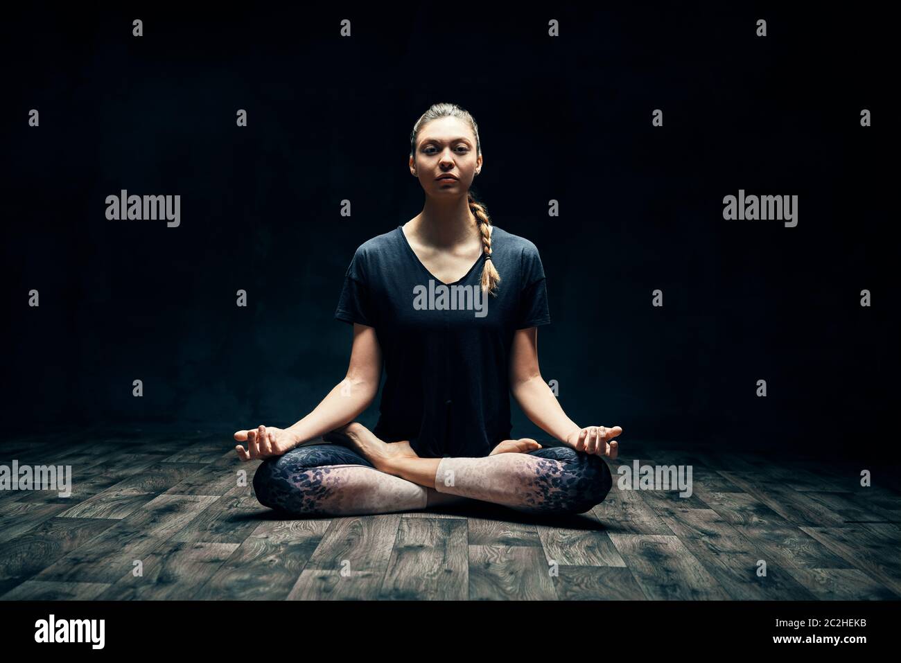 Jeune femme attrayante pratiquant le yoga assis dans la pose de lotus et méditant dans la pièce sombre Banque D'Images