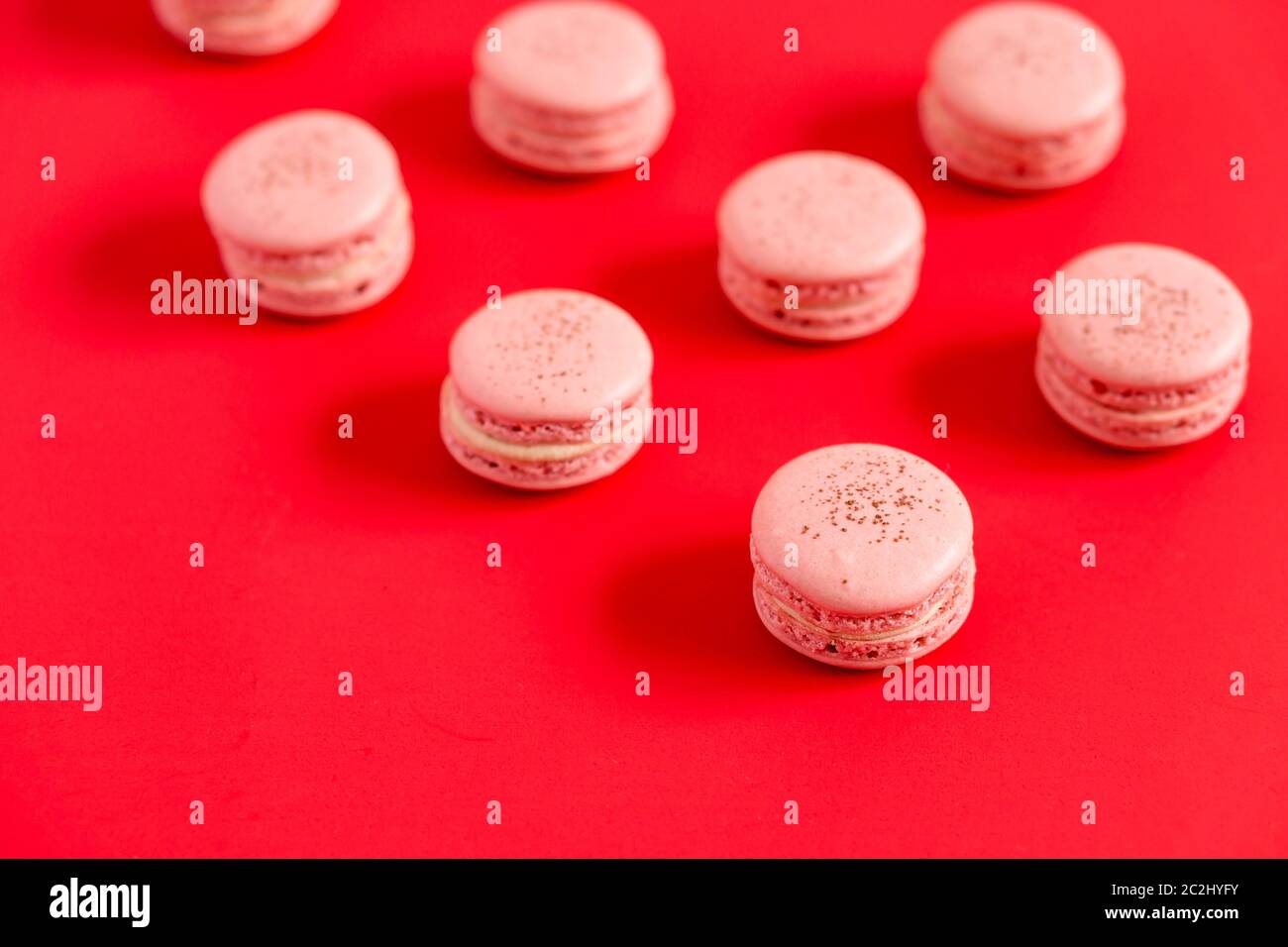 Macarons de fraise sur fond rouge. Ces pâtisseries françaises romantiques sont faites de deux biscuits meringue et d'un sucré. Elles sont légères et nettes. Banque D'Images