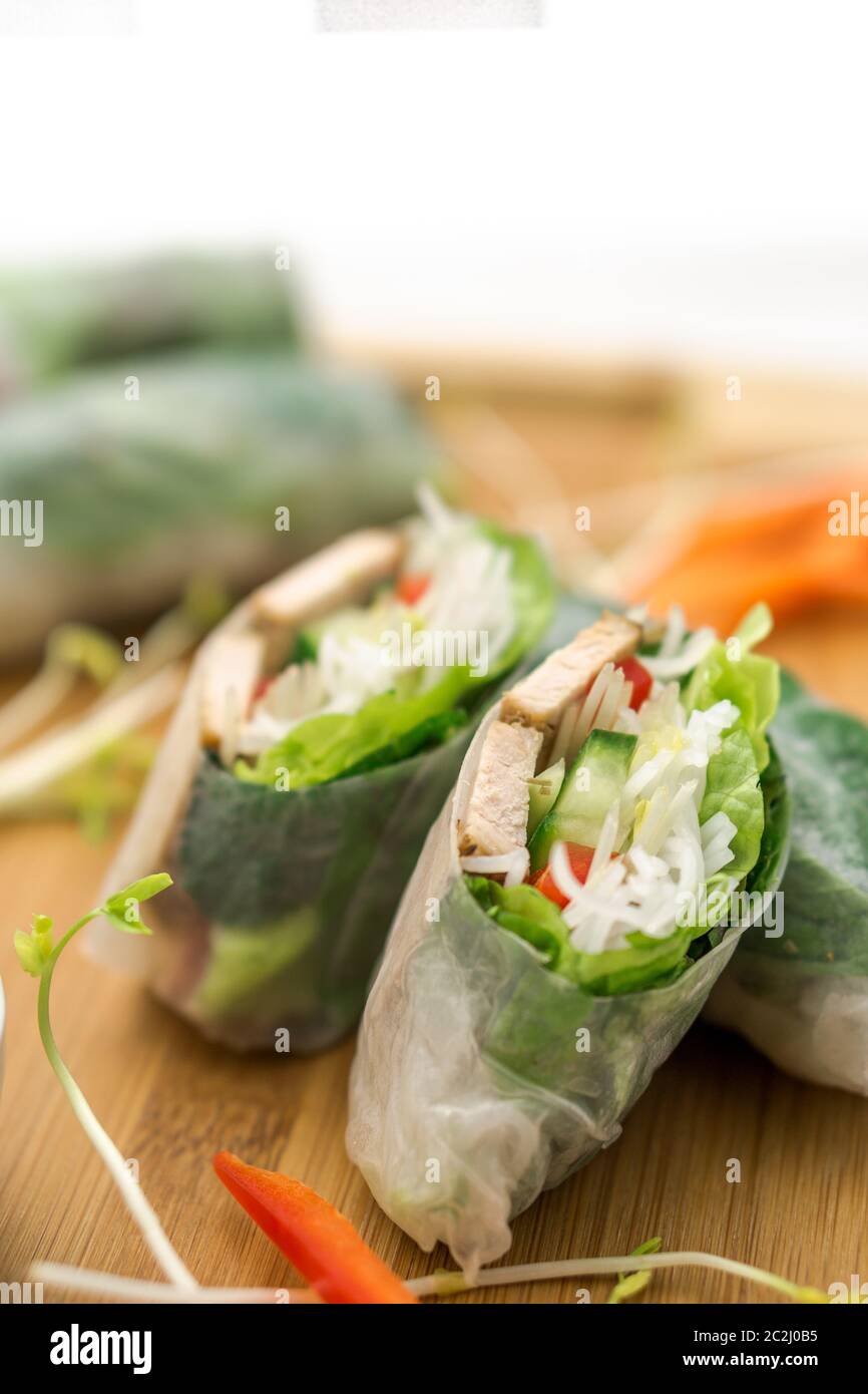 Rouleaux de printemps vietnamiens frais, parfaits comme un apéritif sain avec une sauce au beurre d'arachide pour tremper. La nourriture est placée sur une planche à découper en bois. Banque D'Images