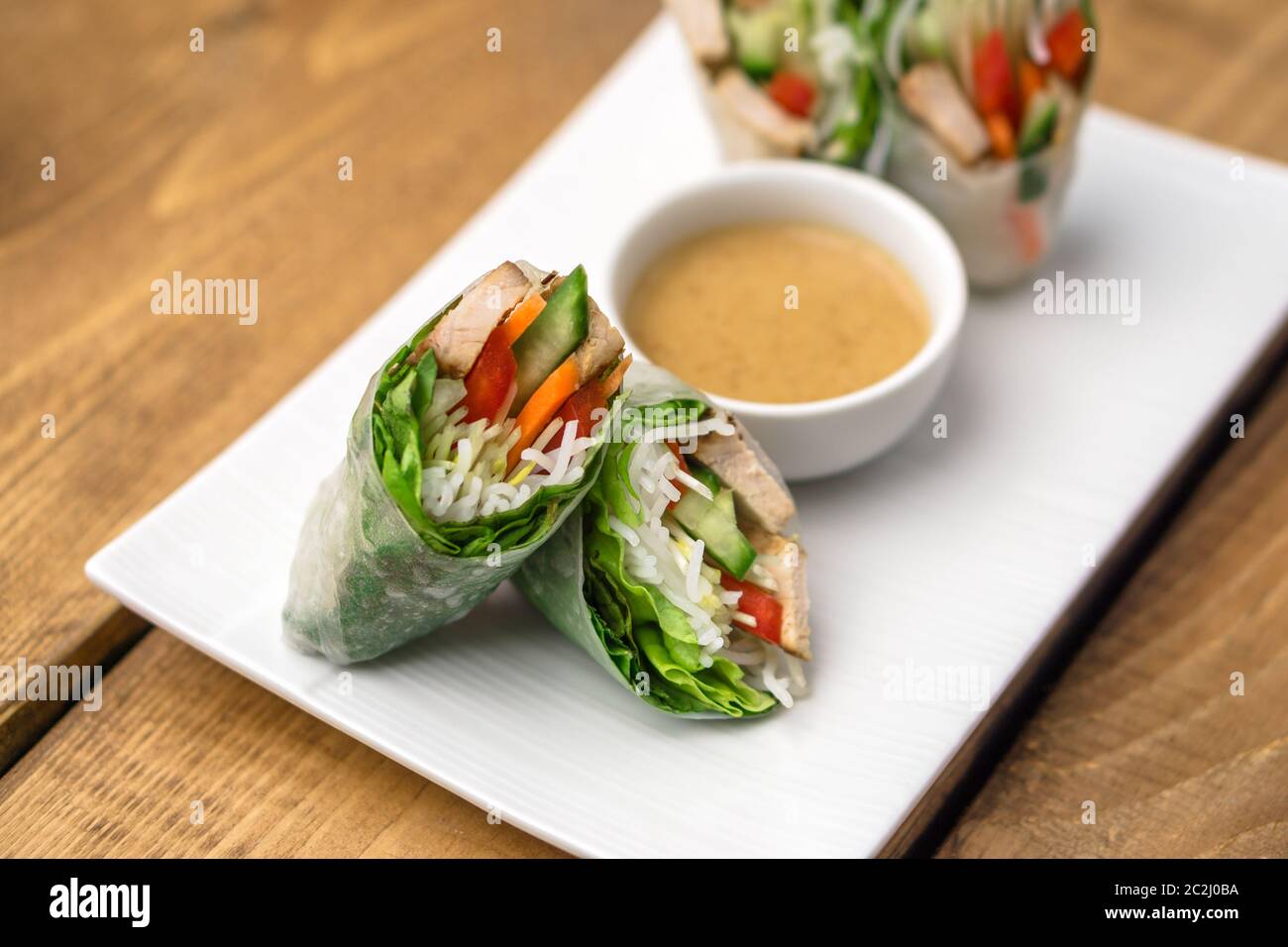 Rouleaux de printemps vietnamiens frais, parfaits comme un apéritif sain avec une sauce au beurre d'arachide pour tremper. La plaque est placée sur un fond en bois. Banque D'Images