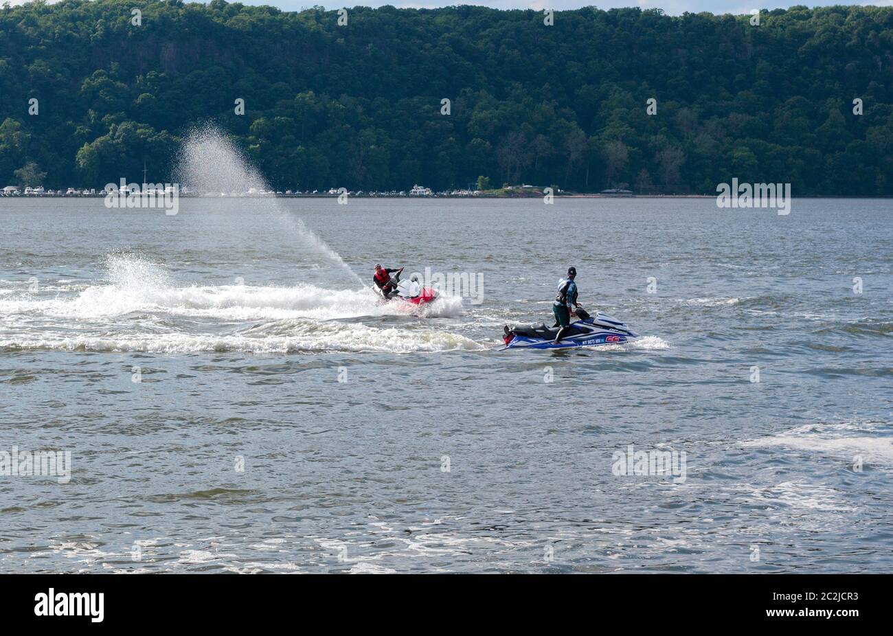 Deux hommes font des tours sur des motomarines sur l'Hudson River dans le nord de Manhattan avec la côte du New Jersey en arrière-plan Banque D'Images