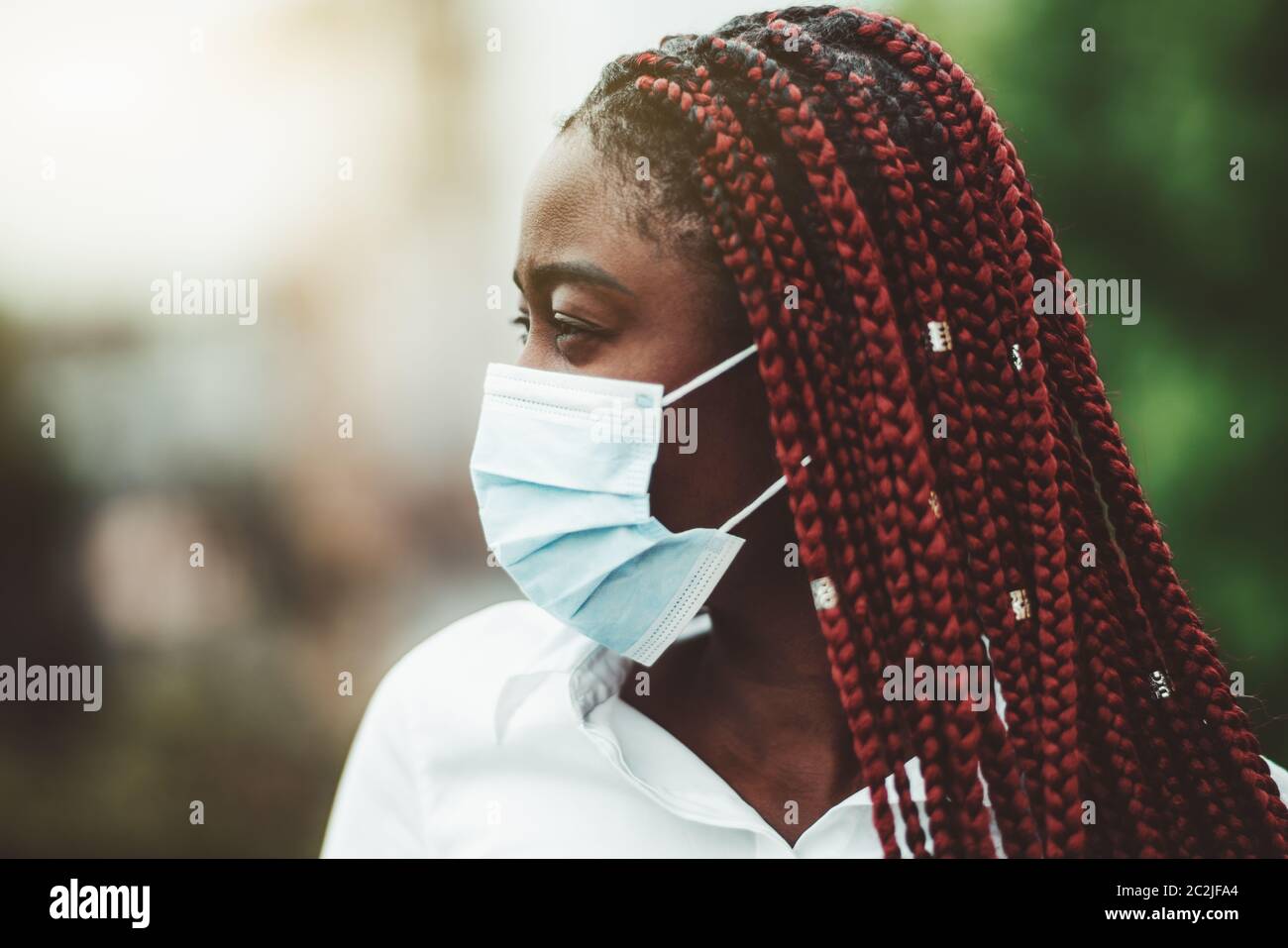 Portrait rapproché d'une jeune femme africaine avec des tresses de châtaignier et dans un masque de protection contre le virus sur son visage; femme noire masquée à l'extérieur - protection Banque D'Images