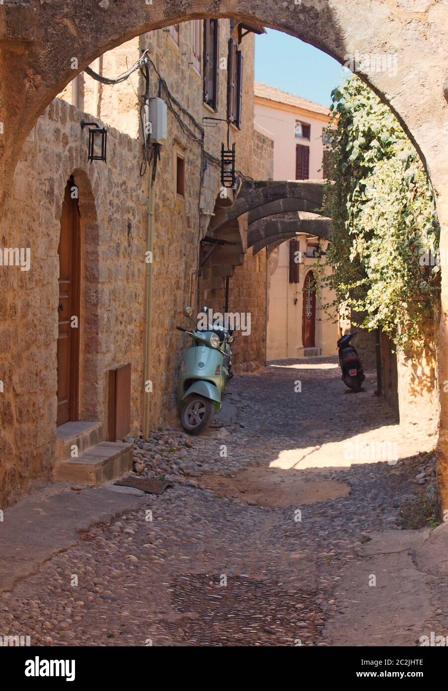 rue pavée calme typique de la ville de rhodes avec de vieilles maisons peintes en jaune et une arche en pierre avec ciel ensoleillé d'été Banque D'Images