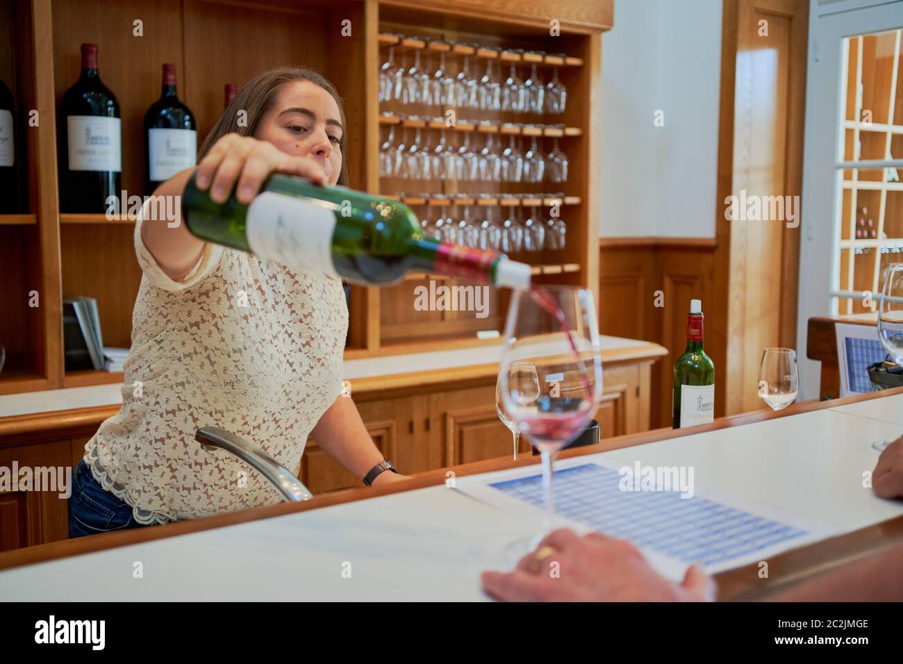 Un membre du personnel sert du vin rouge à un client au comptoir de dégustation de Chateau Lagrange, bouteilles de l'exploitation et verres suspendus, Saint-Julien, France Banque D'Images