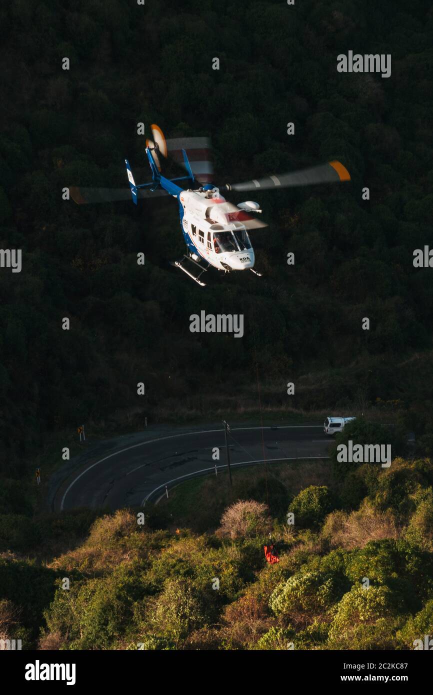Un hélicoptère de sauvetage MBB BK117 abaisse l'équipement sur le site d'une voiture qui est tombée sur une rive abrupte de la route de Byers Pass, Christchurch, Nouvelle-Zélande Banque D'Images Un hélicoptère de sauvetage MBB BK117 abaisse l'équipement sur le site d'une voiture qui est tombée sur une rive abrupte de la route de Byers Pass, Christchurch, Nouvelle-Zélande Banque D'Images