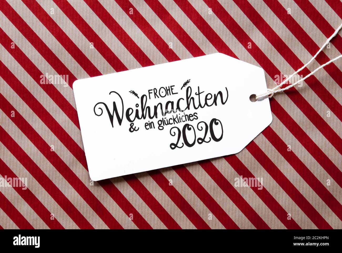 L'étiquette avec la calligraphie allemand Frohe Weihnachten und ein 2020 Glueckliches veut dire Joyeux Noël et une Bonne 2020. Papier d'emballage rouge en arrière-plan Banque D'Images