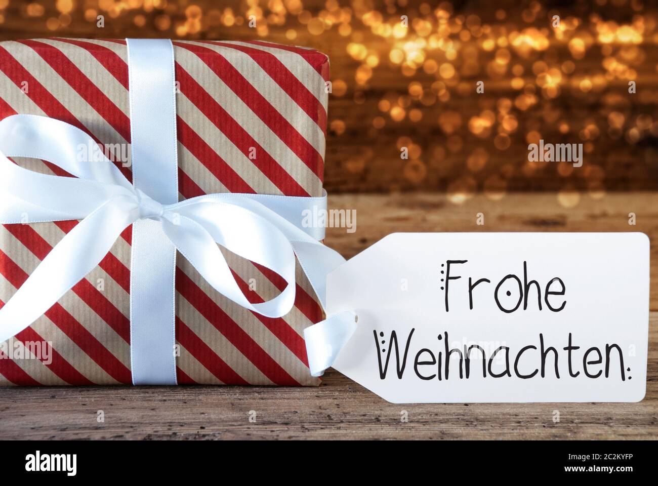 Un cadeau de Noël avec étiquette avec calligraphie allemand Frohe Weihnachten signifie joyeux Noël. Du papier d'emballage avec un arc et des lumières en arrière-plan Banque D'Images
