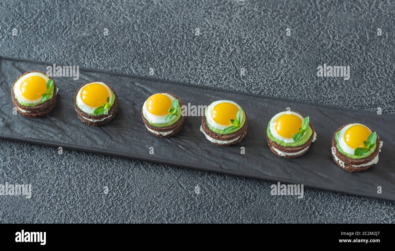 Canape avec fromage à la crème, guacamole et oeufs de caille frit sur la plaque Banque D'Images