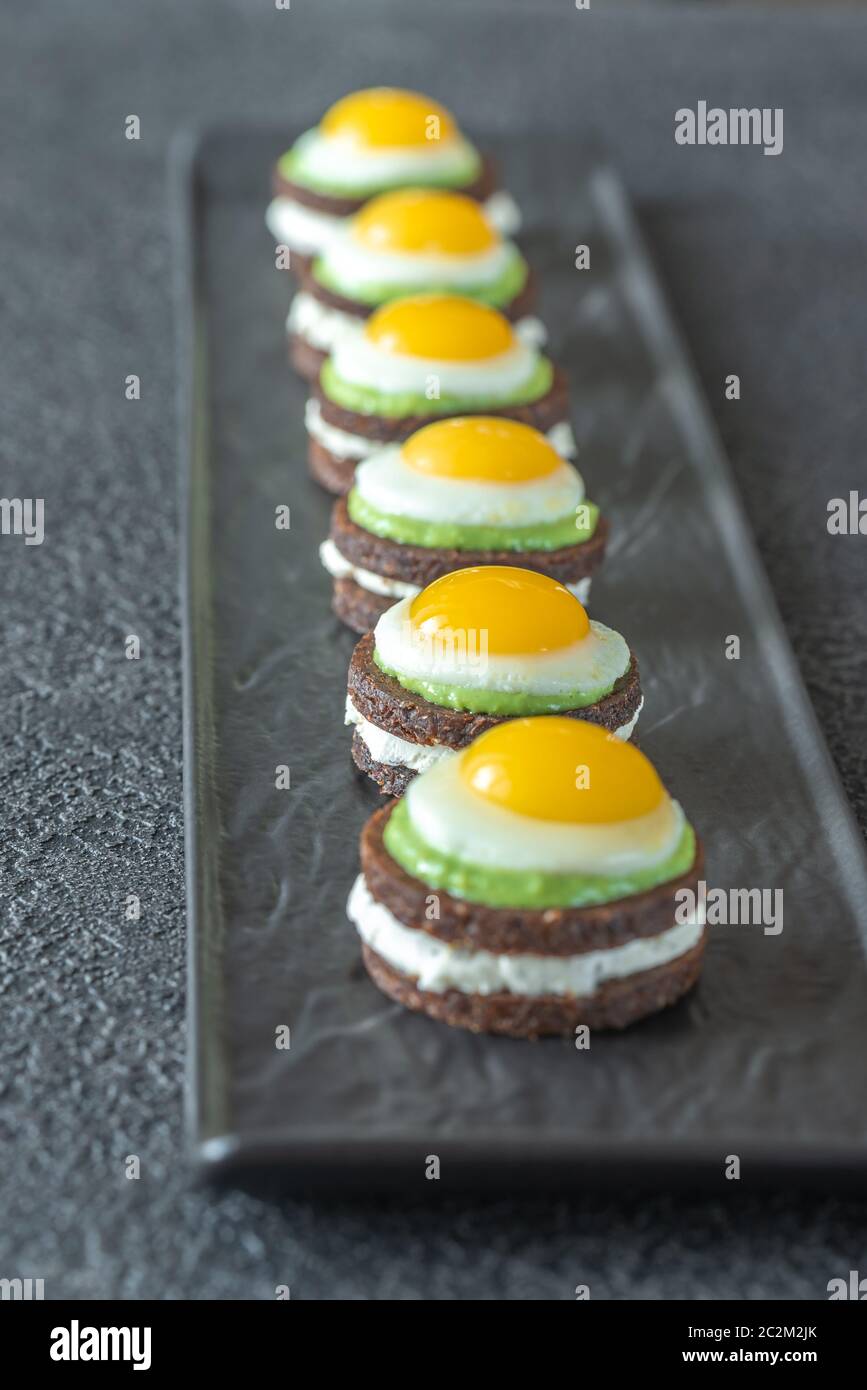 Canape avec fromage à la crème, guacamole et oeufs de caille frit sur la plaque Banque D'Images