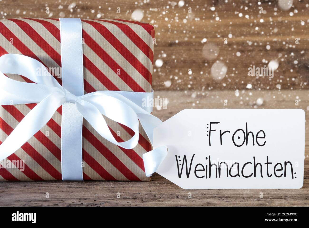 Un cadeau de Noël avec étiquette avec calligraphie allemand Frohe Weihnachten signifie joyeux Noël. Du papier d'emballage avec un arc et des flocons Banque D'Images