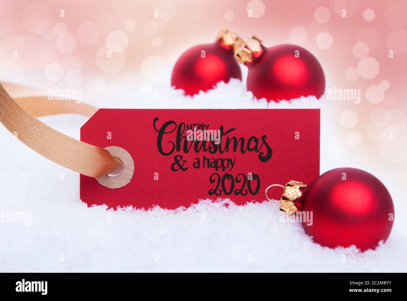 Label Rouge avec calligraphie anglaise Joyeux Noël et une Bonne 2020. Boule de noël ornement. Arrière-plan flou avec de la neige Banque D'Images