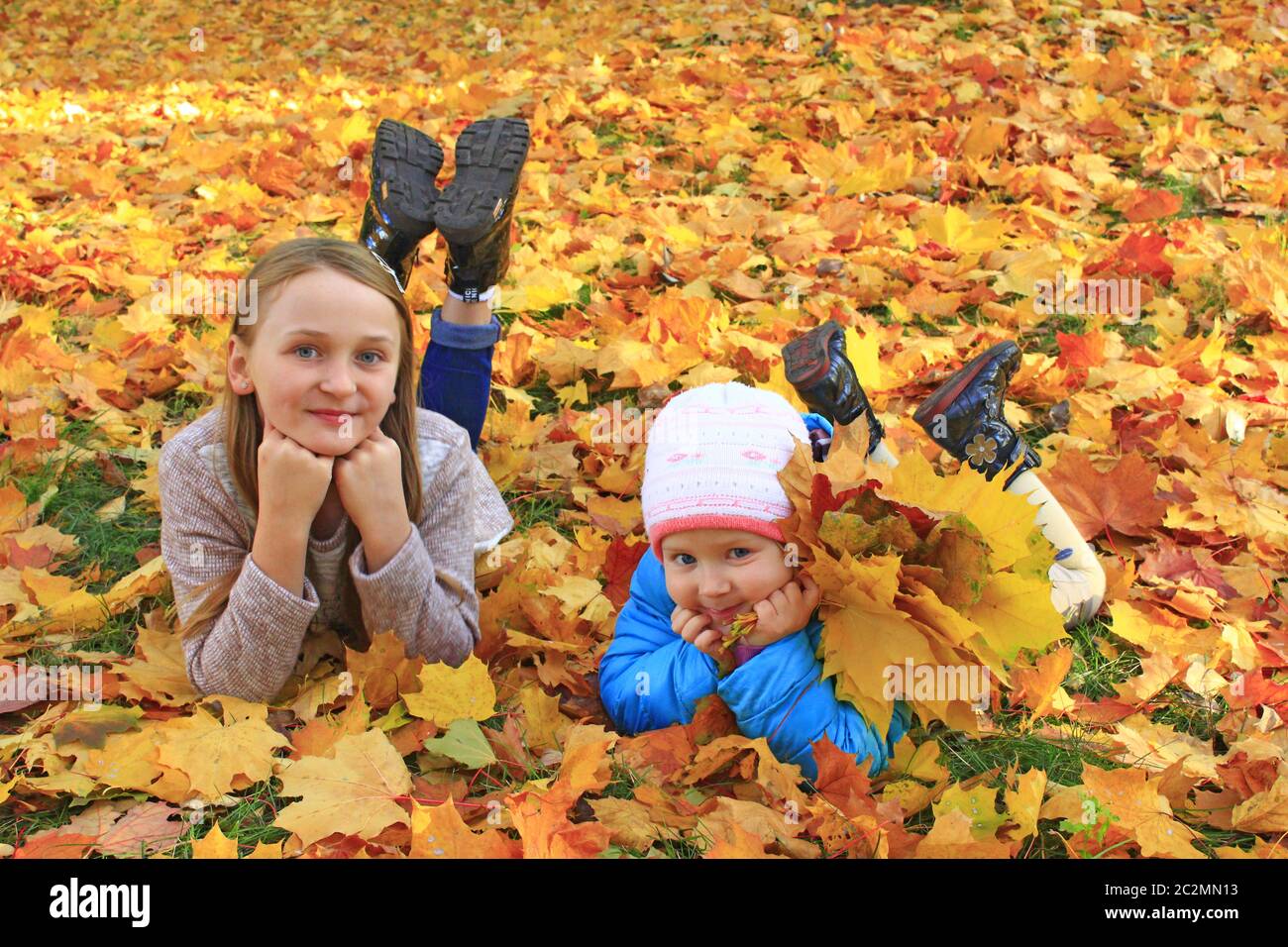 Adorables petits enfants jouant dans le parc d'automne. Jeunes sœurs qui ponent sur des feuilles jaune et orange vives Banque D'Images