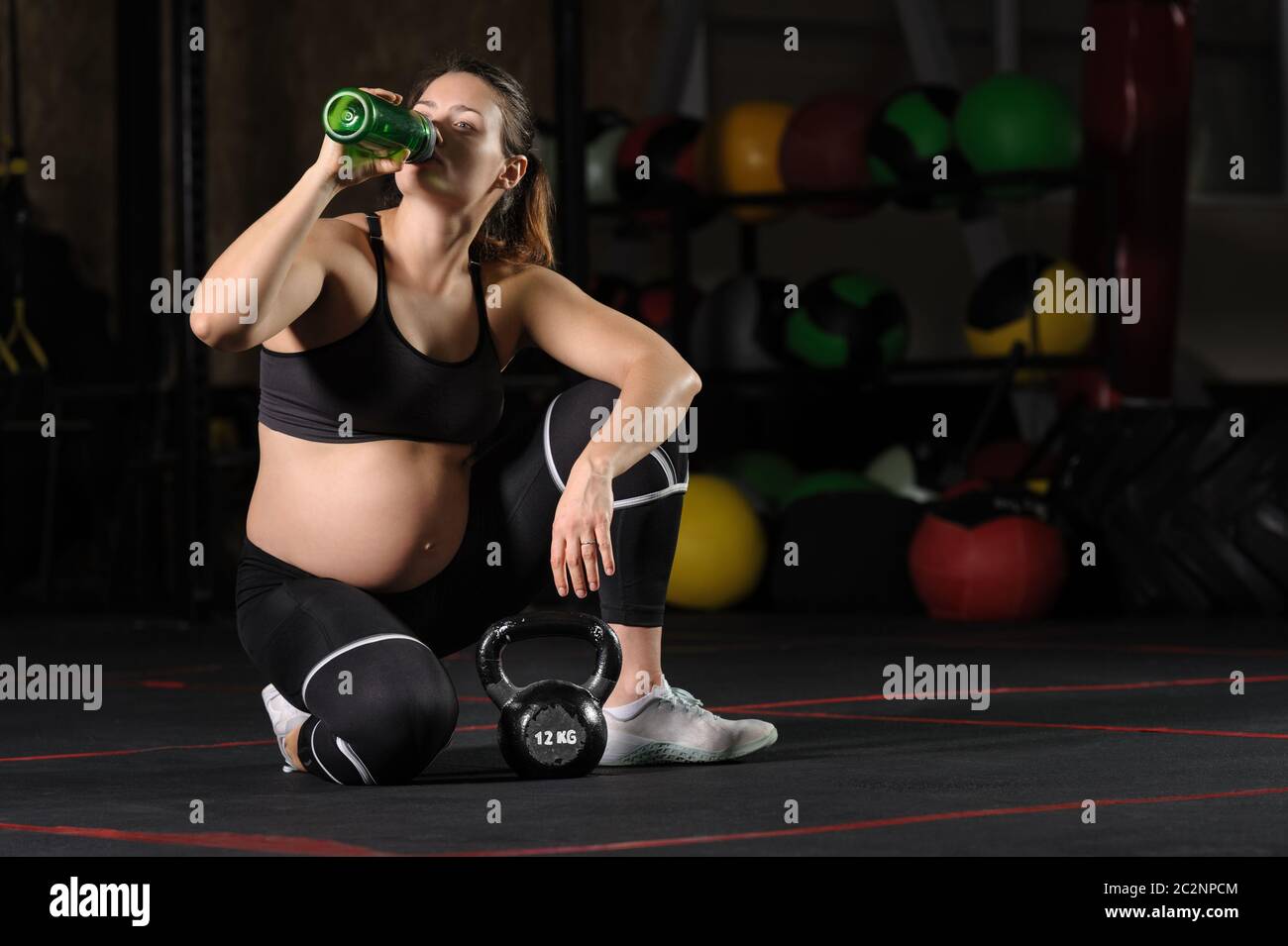 Jeune femme enceinte de boire wate à partir de bouteille en plastique dans la salle de sport Banque D'Images