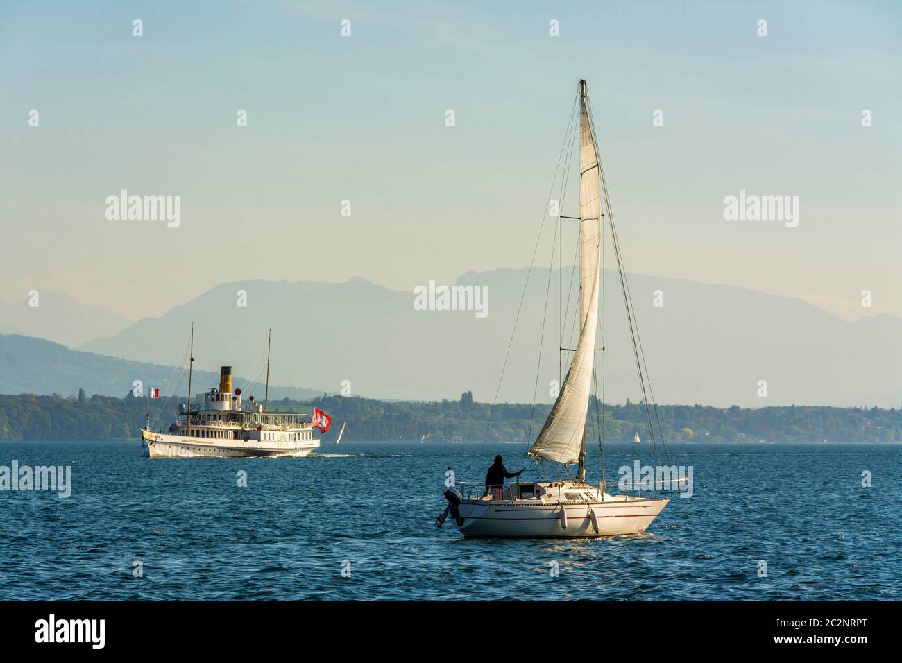 Le bateau à aubes Savoie approche du port de Nyon à Vaud, en Suisse, tandis qu'un voilier navigue sur les eaux calmes, en Suisse Banque D'Images