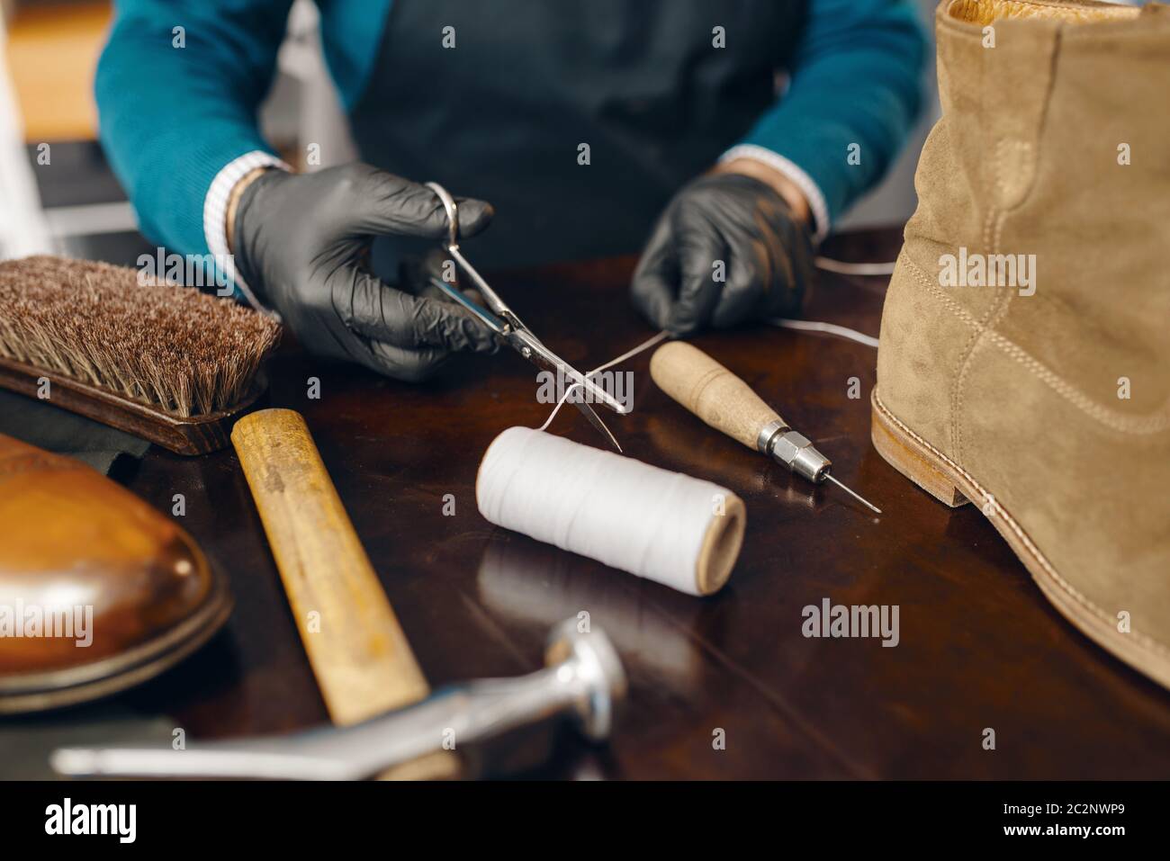 Le cordonnier coupe le fil, le service de réparation de chaussures. Compétence d'artisan, atelier de fabrication de chaussures, maître travaille avec des bottes, travail de cordonnier Banque D'Images