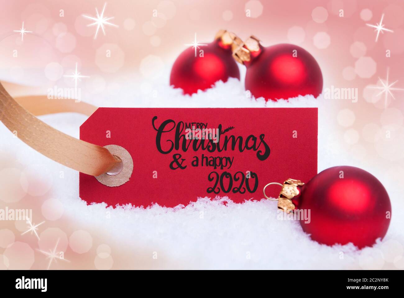 Label Rouge avec calligraphie anglaise Joyeux Noël et une Bonne 2020. Boule de noël ornement. Flou d'arrière-plan avec la neige brillant Banque D'Images