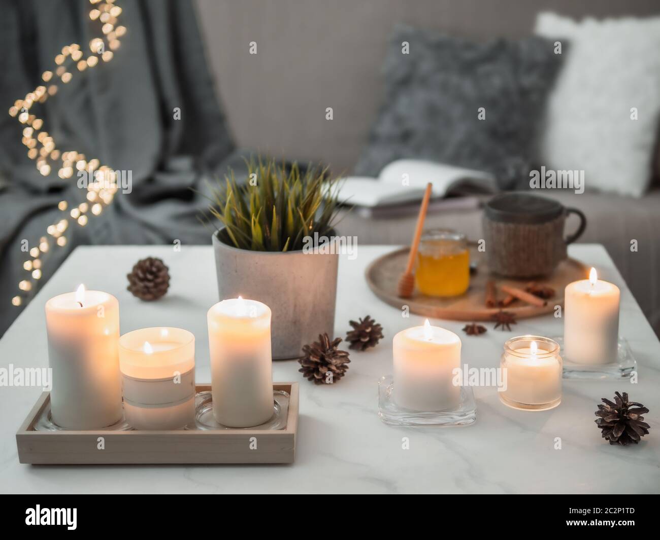 Maison confortable, hygge, concept de coziness - bougies parfumées blanches sur table en marbre blanc près du canapé avec oreillers et écossais. Décoration d'hiver, tasse à thé chaude Banque D'Images