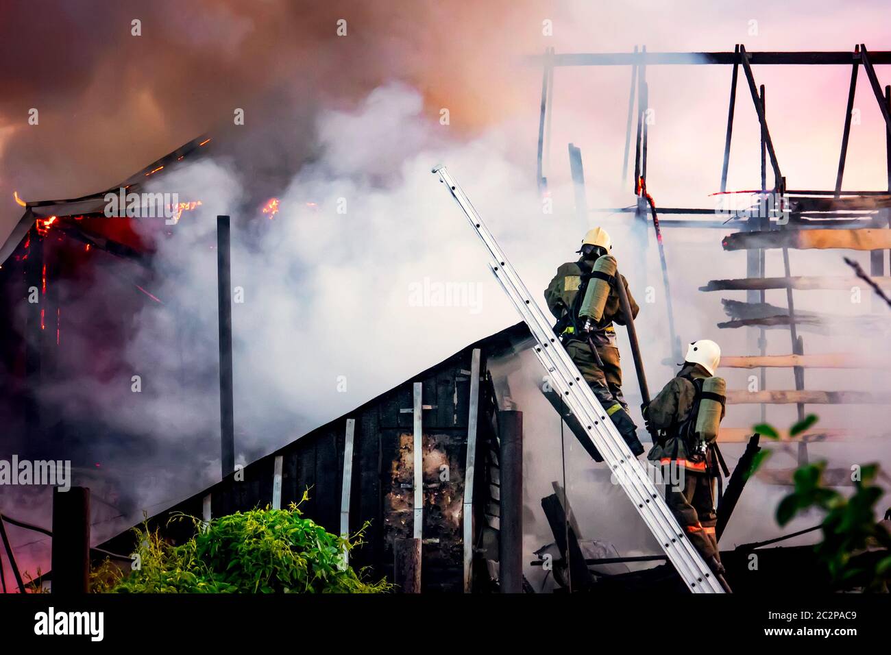 les pompiers combattent un feu de forêt sur fond de fumée blanche épaisse. Les pompiers des escaliers éteignent le toit d'une maison privée ou d'une grange. Banque D'Images