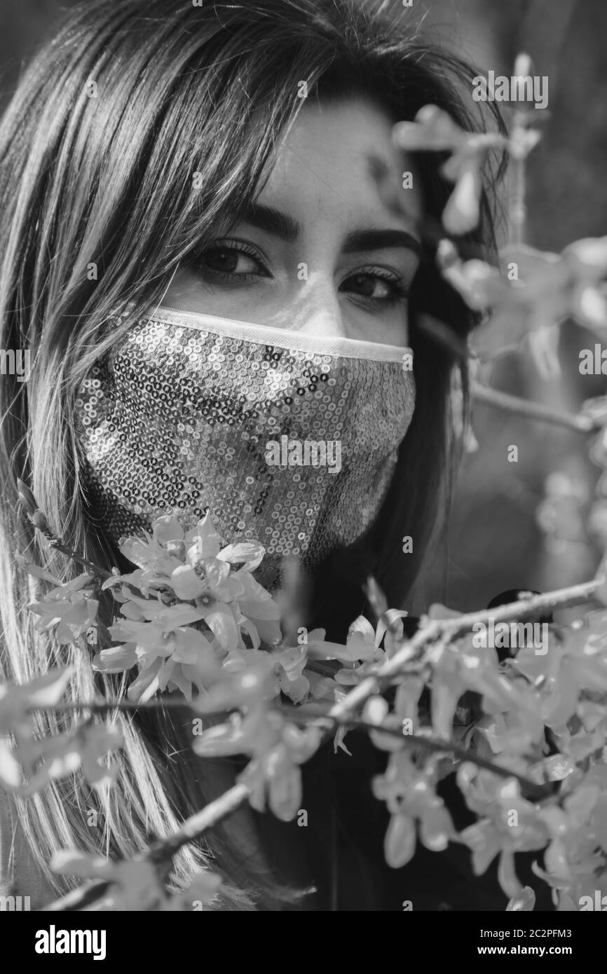 jeune femme sérieuse avec masque de protection médicale au printemps fleurs regarde la caméra, monochrome Banque D'Images