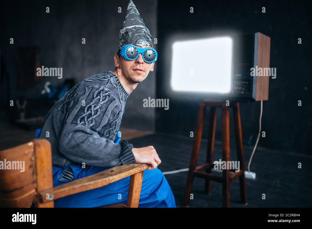 Homme étrange dans le casque de tinfoil et des lunettes hypnotisantes  regarder la télévision, la protection de l'esprit, le concept de paranoïa.  OVNI, théorie du complot, phobie de la télépathie Photo Stock -