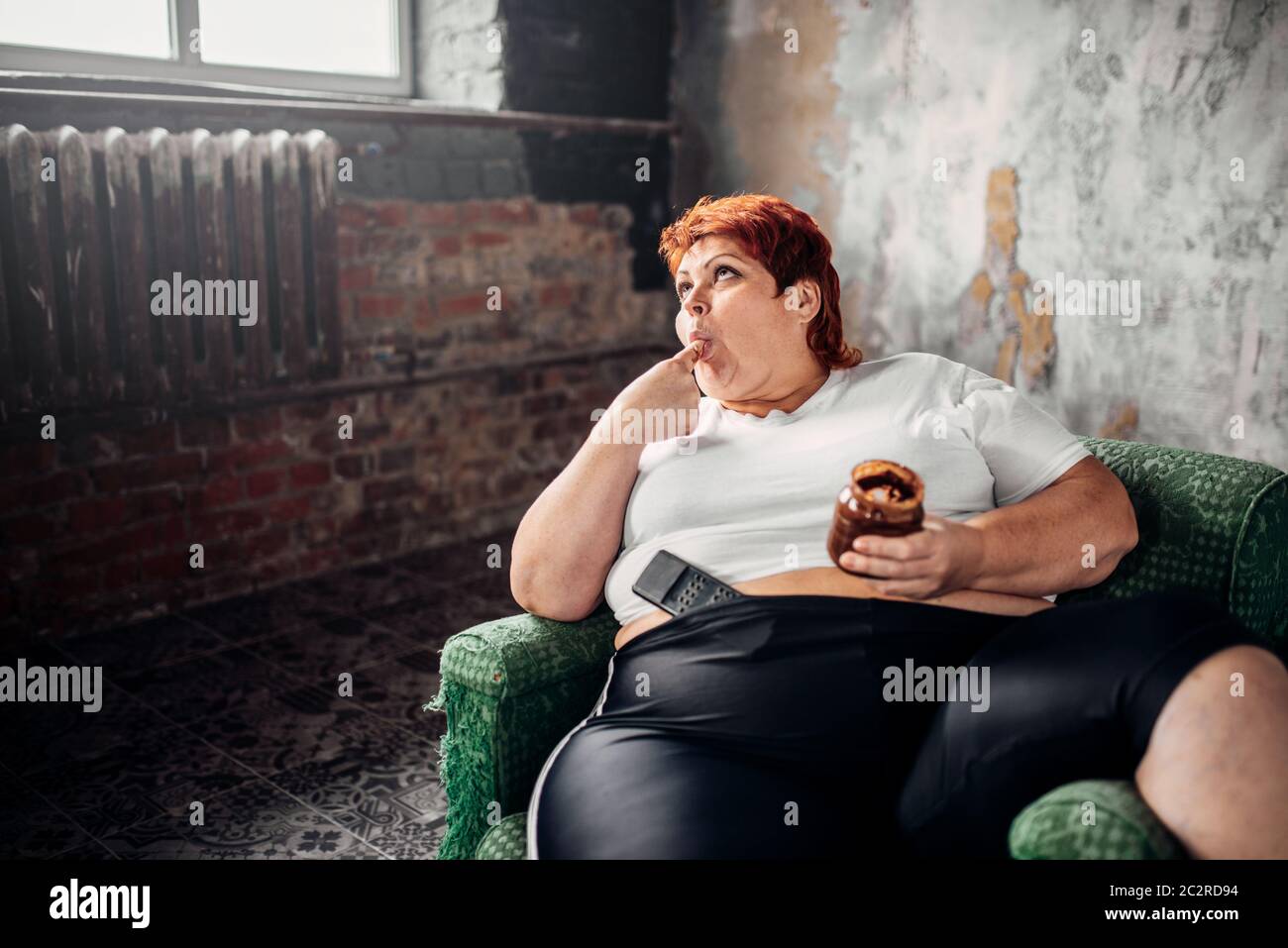 Grosse femme est assise sur une chaise et mange des bonbons, de l'embonpoint. Mode de vie malsain, l'obésité Banque D'Images